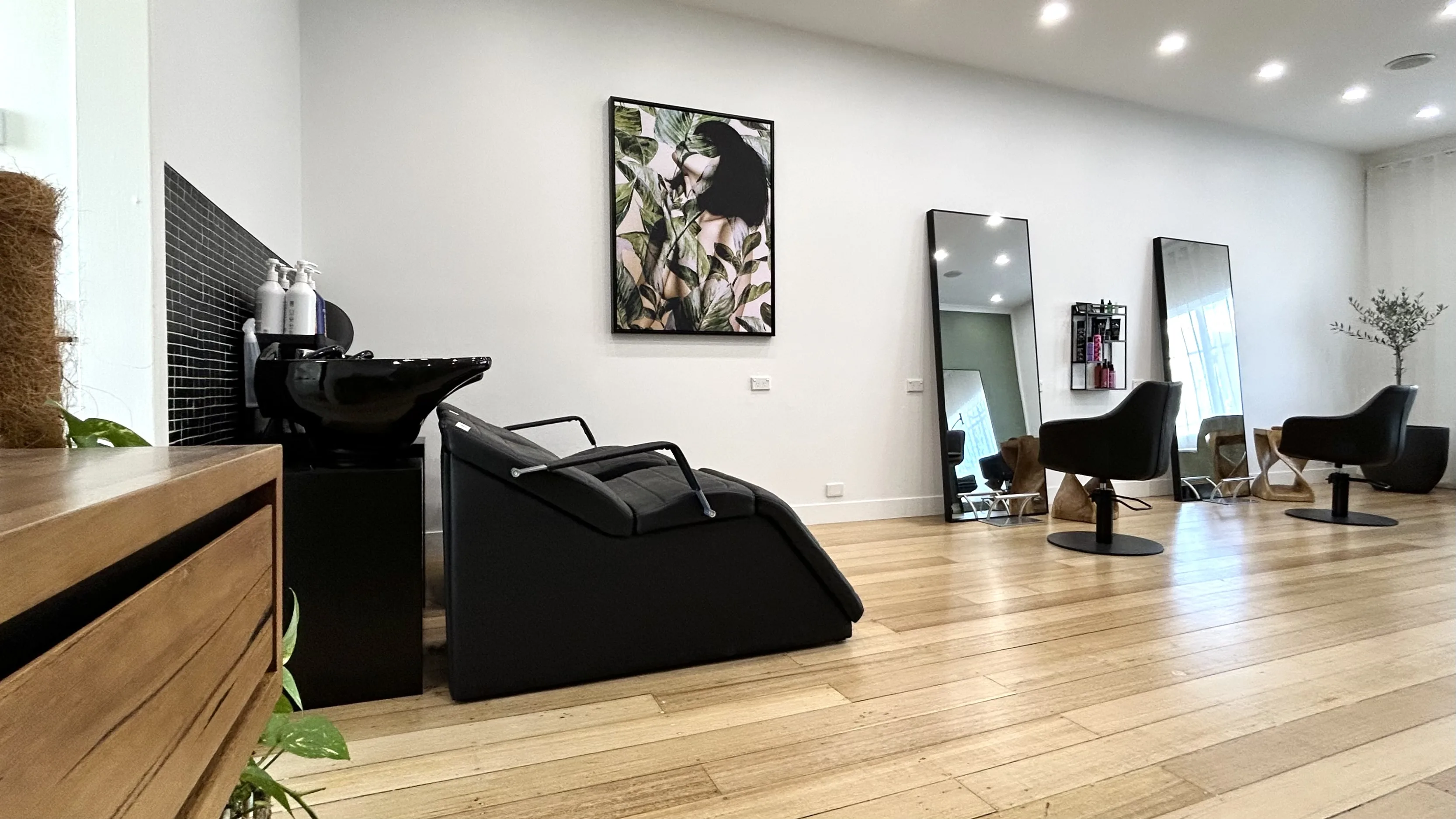 Salon interior — black backwash basin unit, freestanding mirrors, honey timber floor