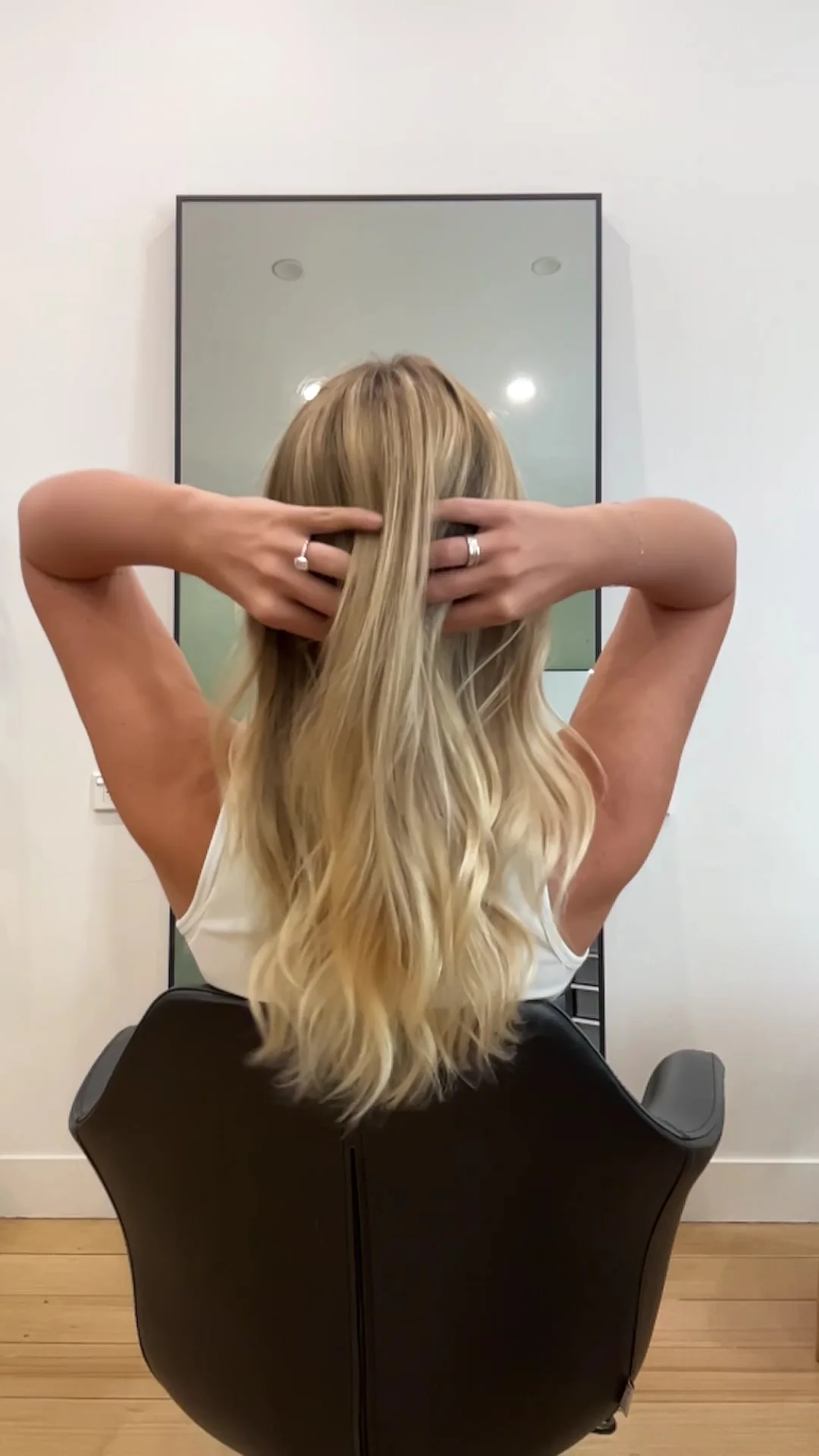 Client lifting long blonde waves before a freestanding mirror