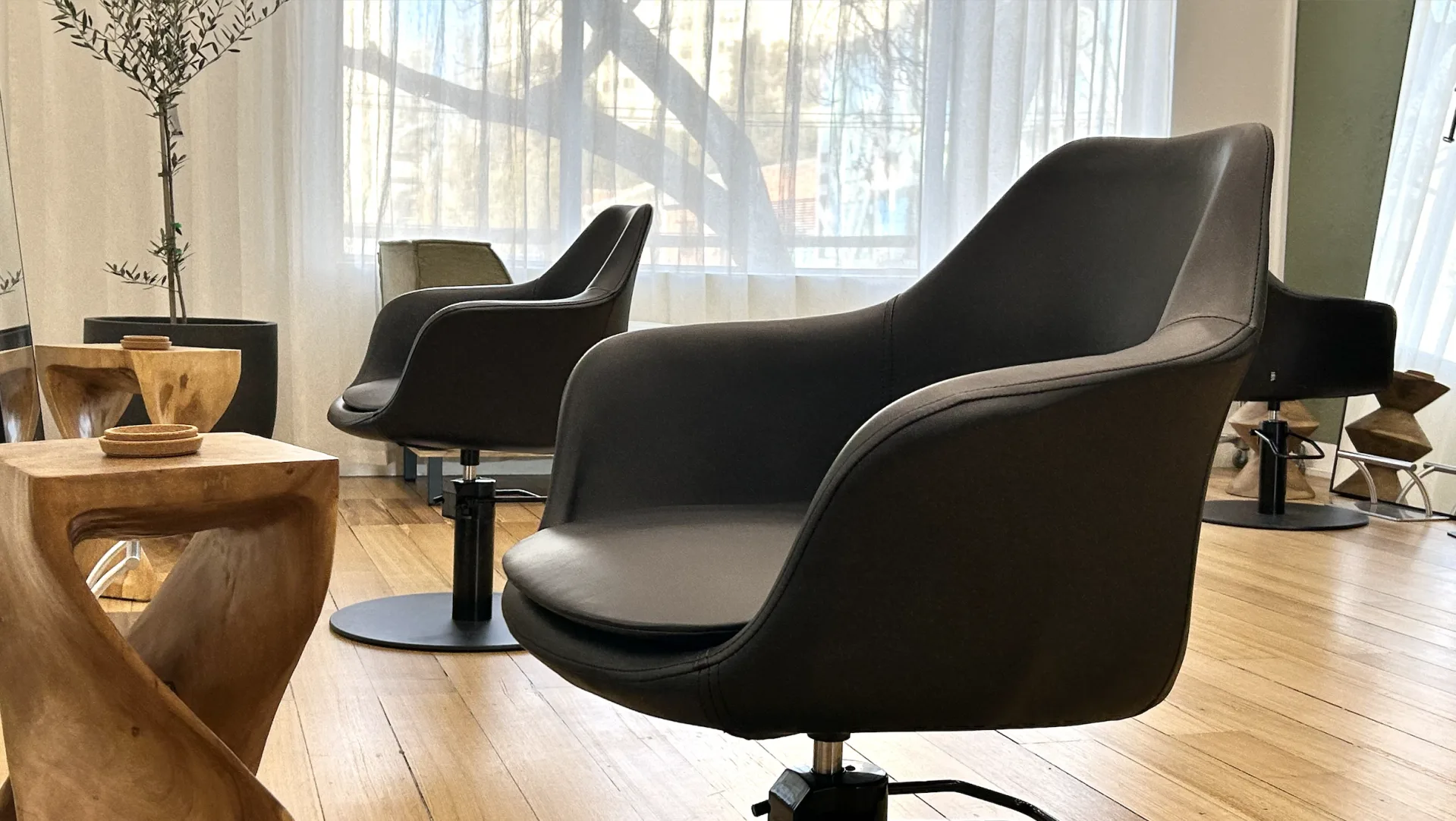 Joey Myers Hair salon — honey timber floors, sheer white curtains, black leather styling chairs on disc bases